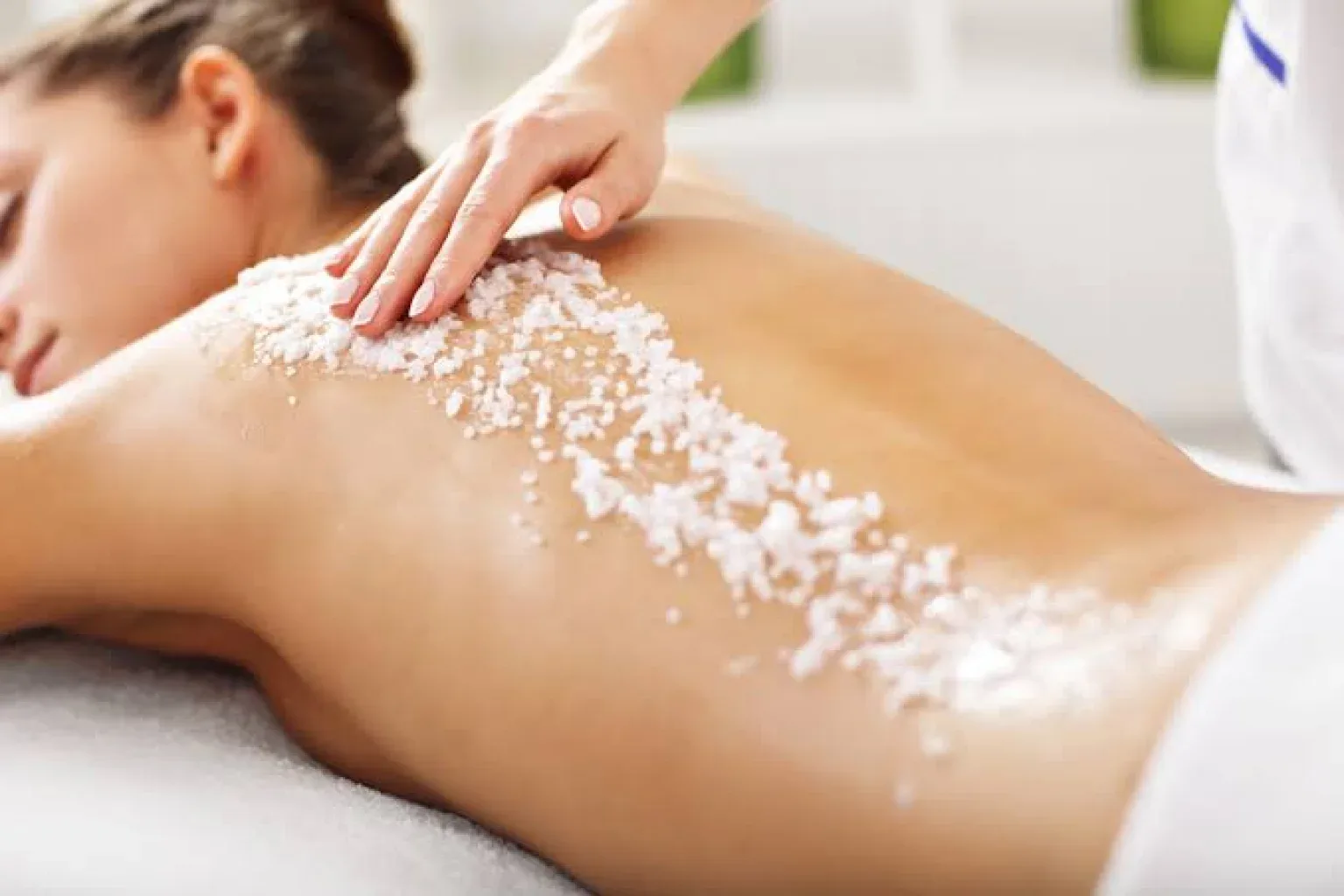 Salt scrub granules being worked across a client's back in a bright treatment room