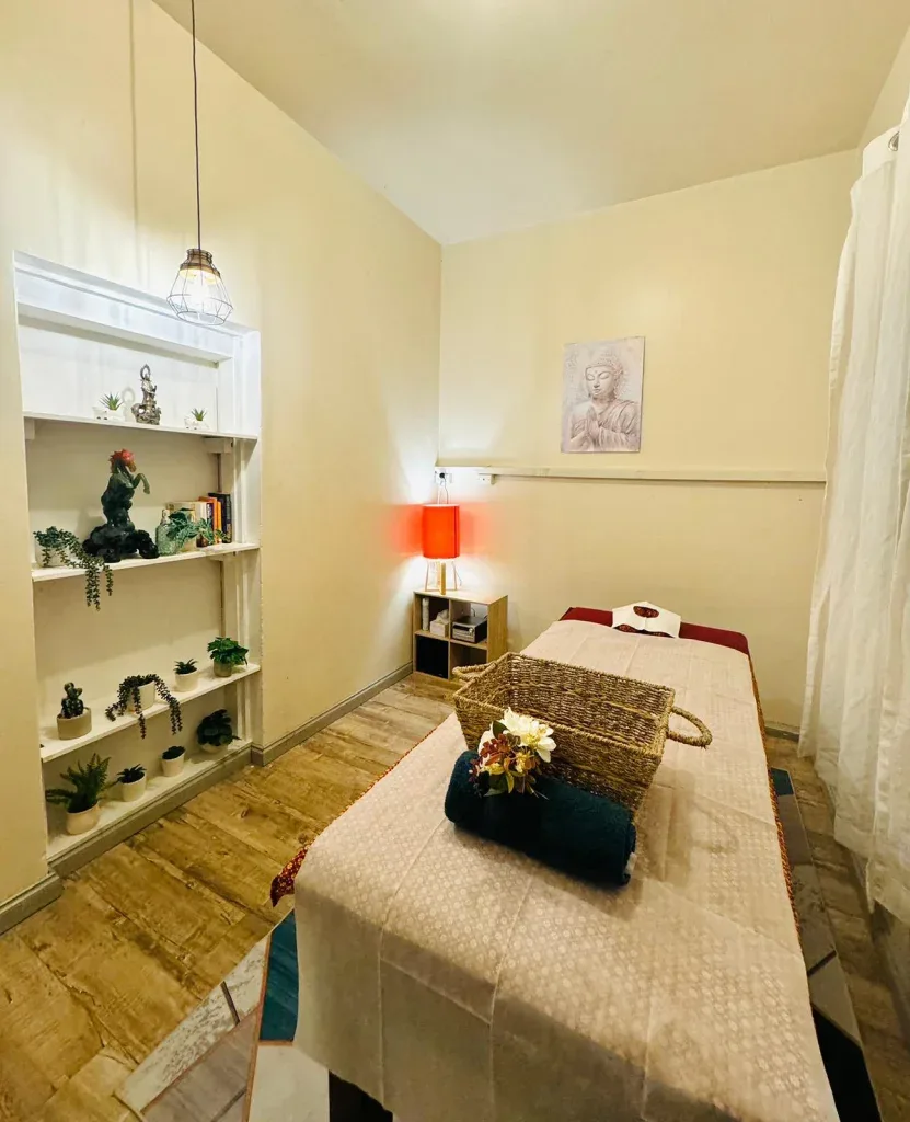 The real single treatment room — made-up table, shelving with plants and Buddha figures, warm red lamp, timber floor