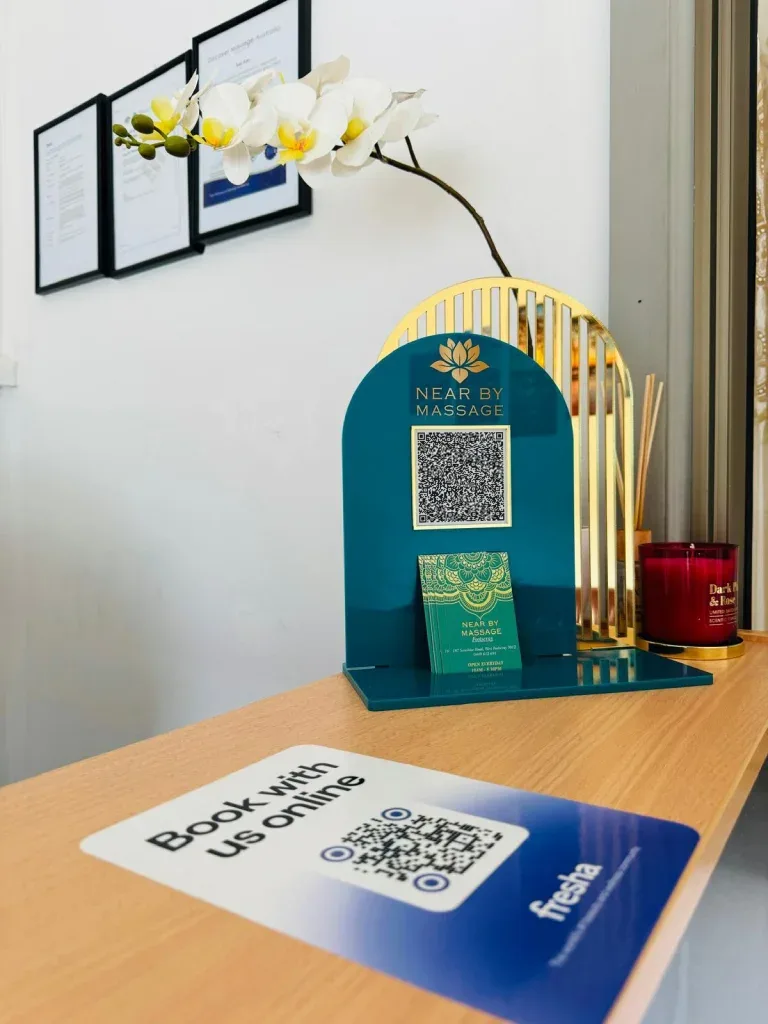 The reception counter — a teal and gold Fresha QR stand, Book with us online card, framed certificates on the wall, orchid